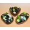 Examples of three handmade acacia bowls displaying a green and natural colored blend of botanicals. Bowl shapes are heart, oval, and shell.
